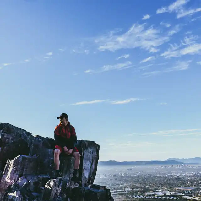 Hiker seated on a rocky mountain ledge overlooking the Phoenix metropolitan area
