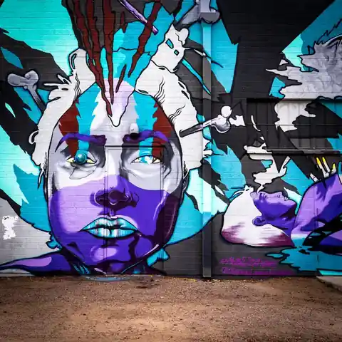 Large turquoise and purple street-art portrait painted across a brick building