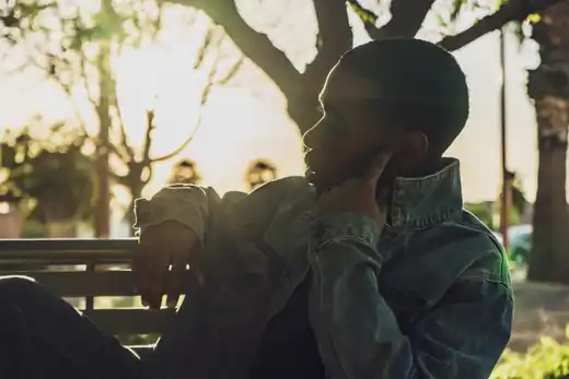 Contemplative portrait of a man in a denim jacket seated on a park bench